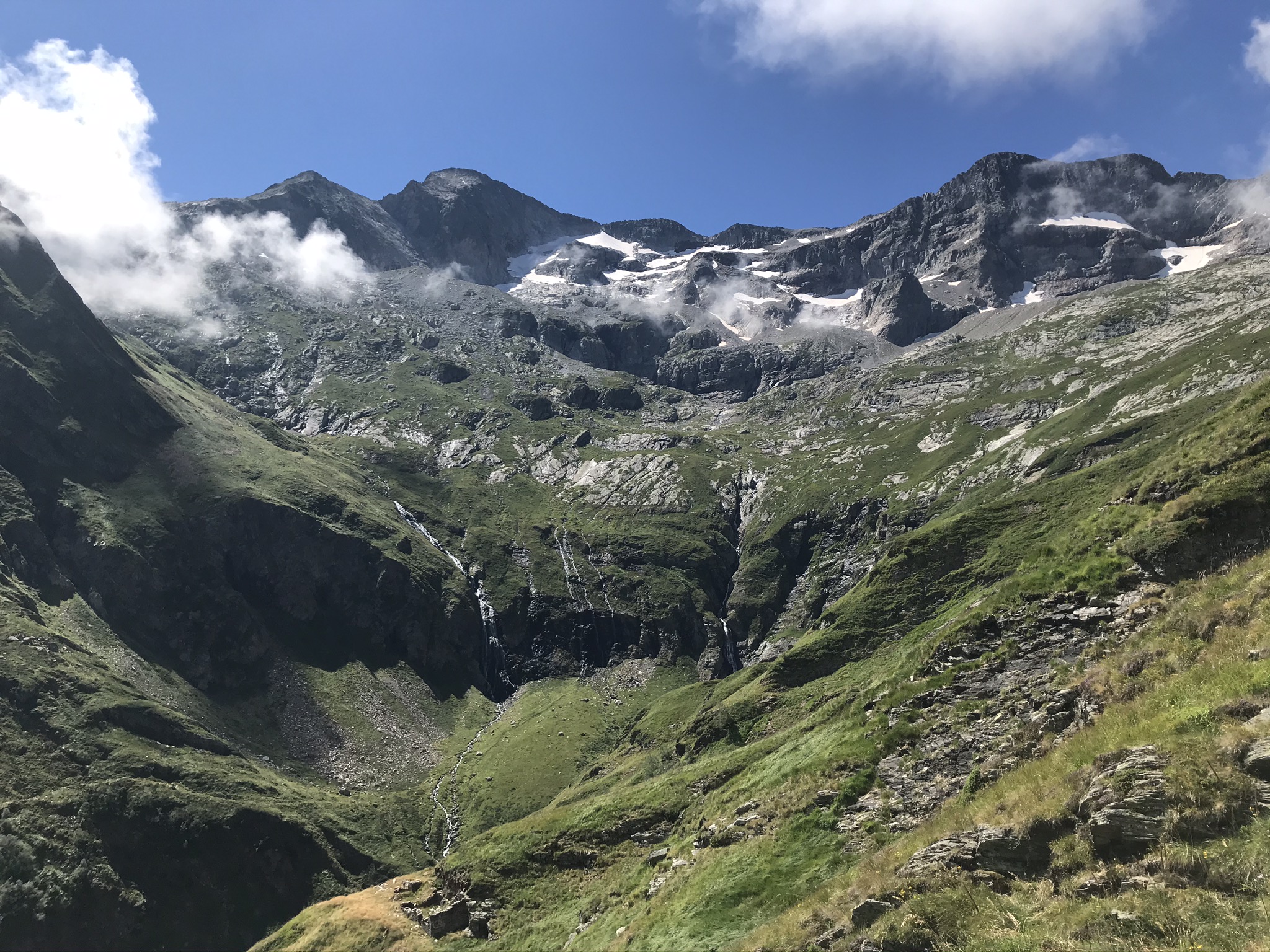 Cirque naturel escarpé avec parois rocheuses, petites cascades de fonte des neiges et névés sous un ciel bleu dans les Pyrénées près de Luchon.