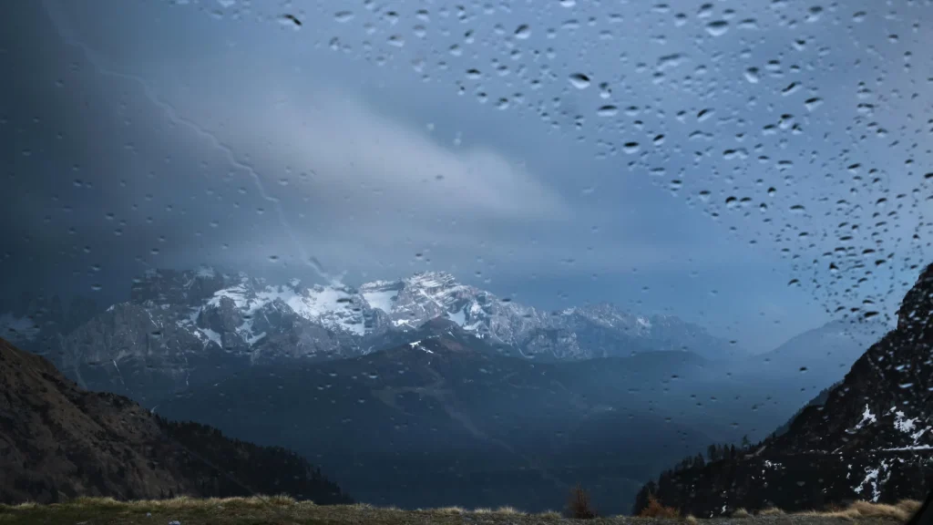 Sommets enneigés des Pyrénées aperçus à travers une vitre couverte de gouttes de pluie, ambiance mélancolique et chaleureuse à Luchon.