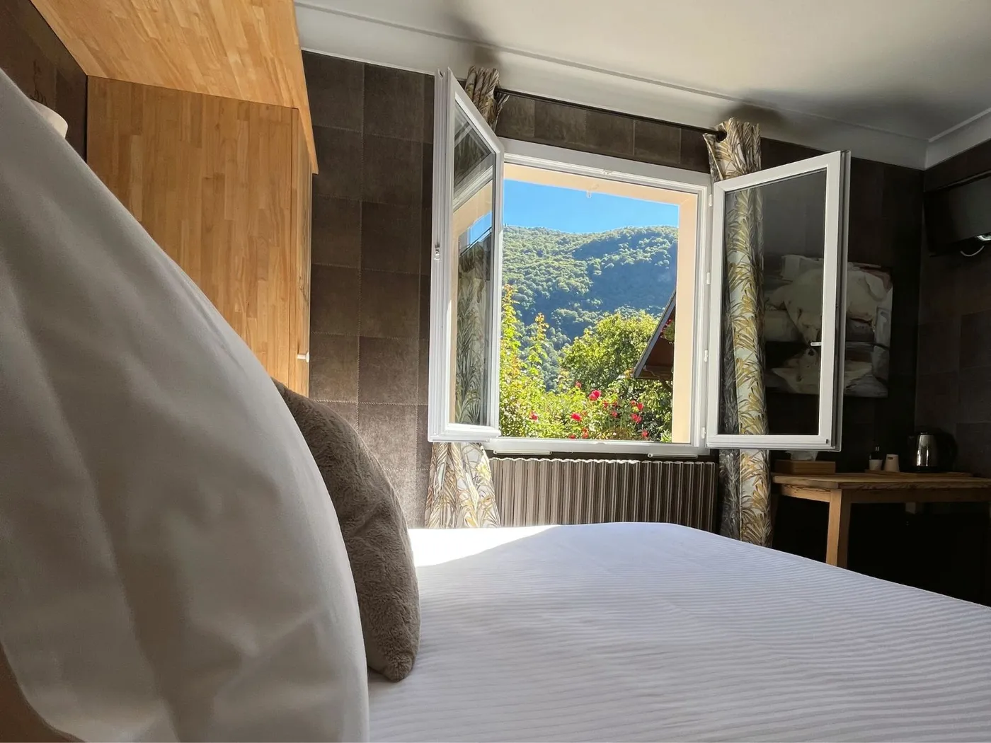 Perspective depuis le lit de la chambre 31 montrant la fenêtre ouverte sur les montagnes verdoyantes des Pyrénées.