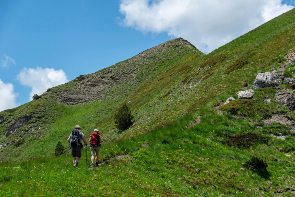 Deux randonneurs équipés marchant sur un sentier de crête herbeux dans les montagnes du Luchonnais, Pyrénées.