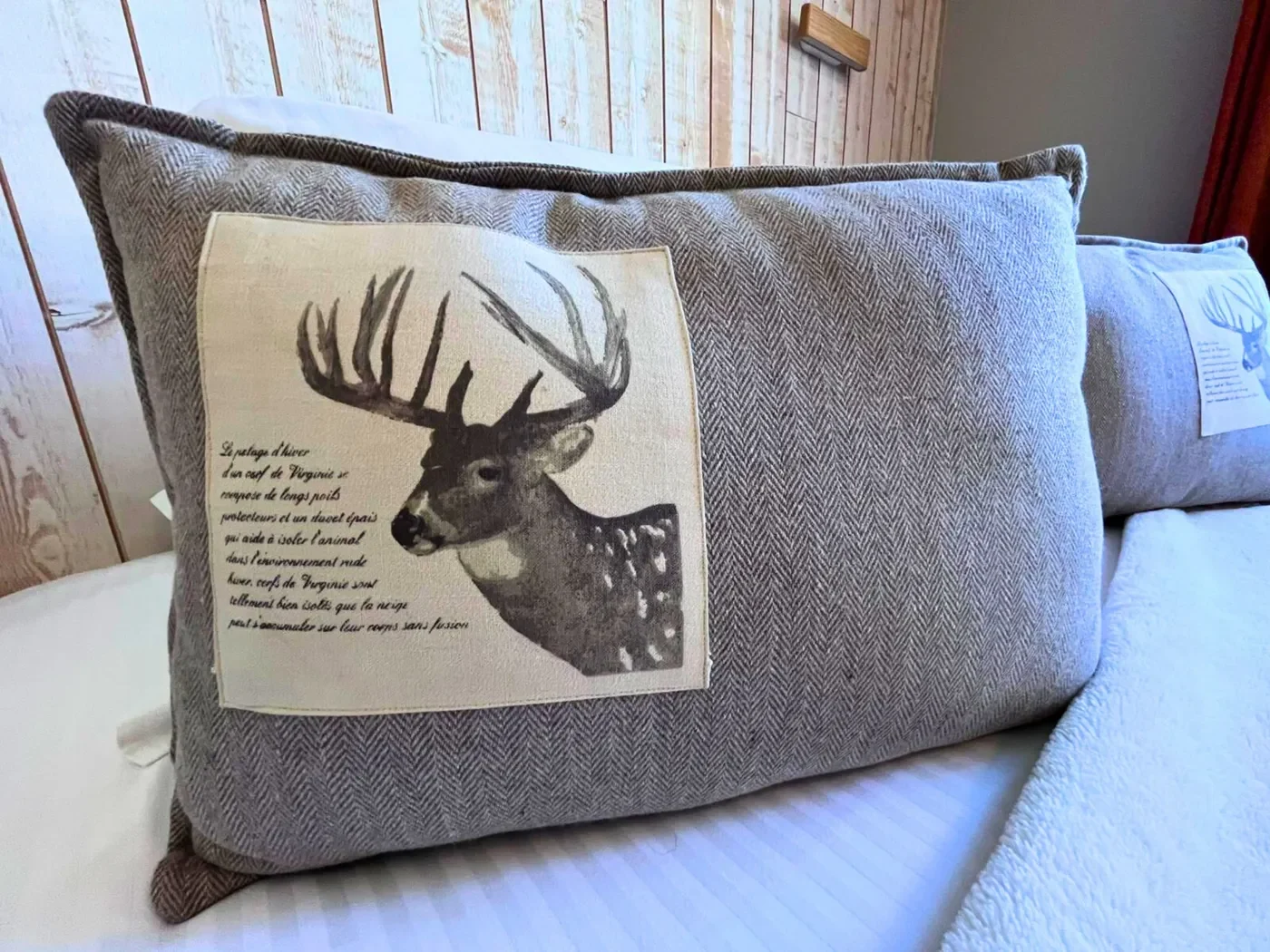 Détail de la literie en chambre n°6 avec coussins brodés d'une tête de cerf sur fond de bois clair.