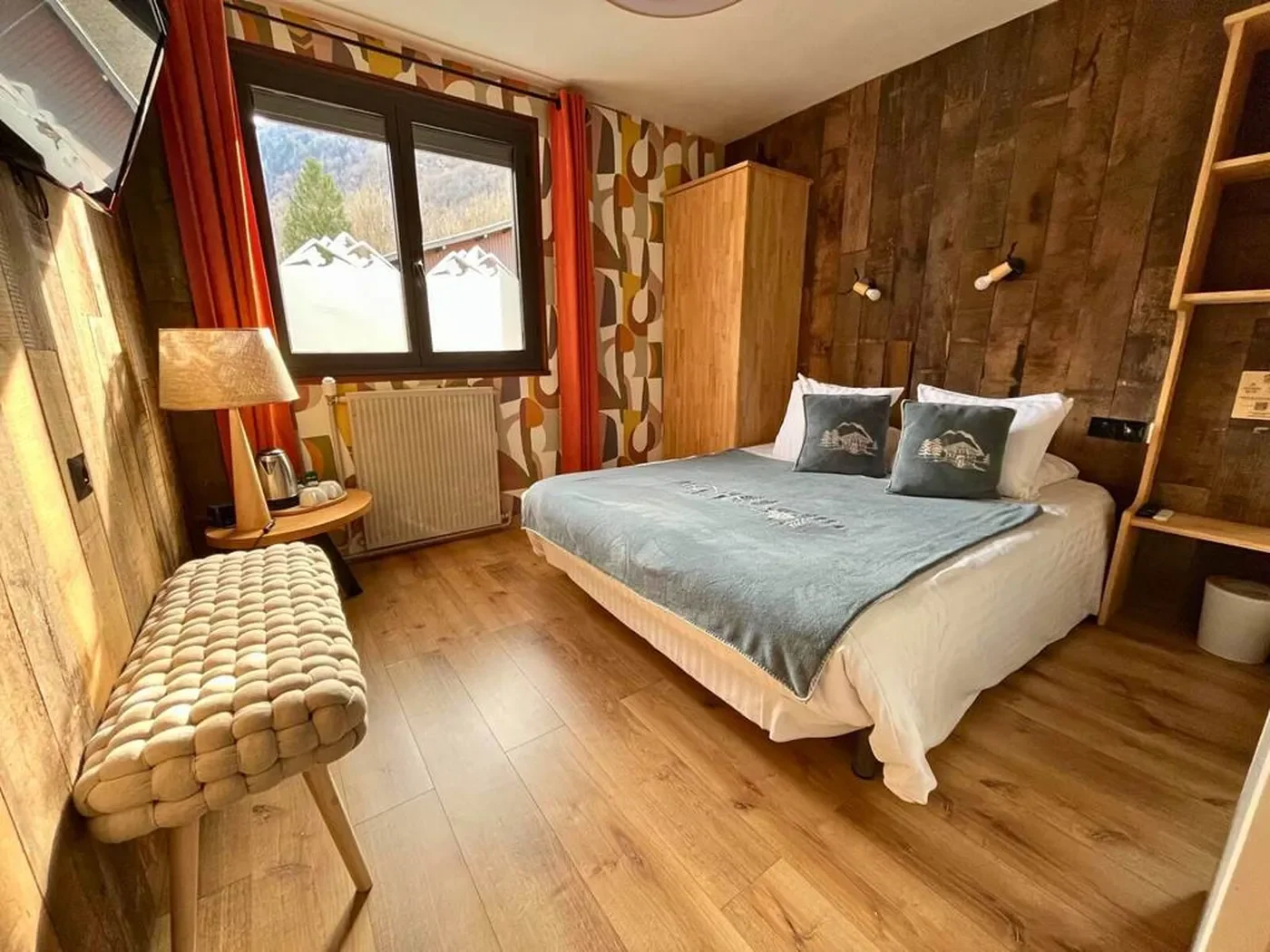 Vue d'ensemble de la chambre double n°2 avec mur en bois massif, papier peint géométrique rétro, lit queen-size et banc tressé.