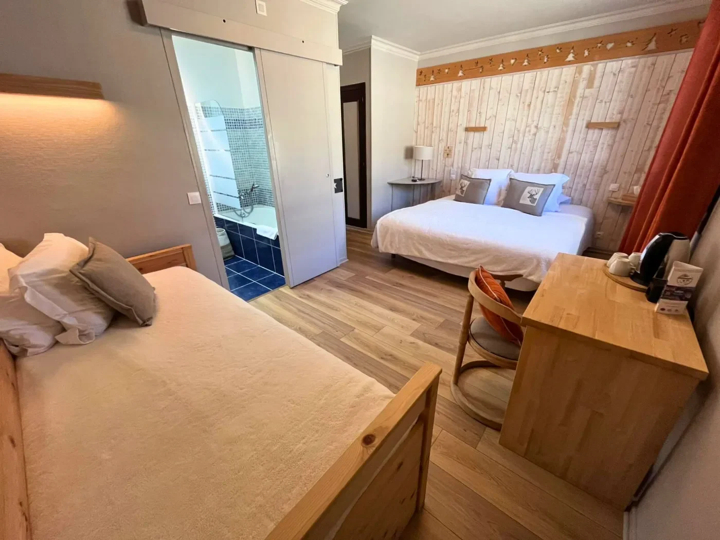 Vue depuis la chambre n°6 vers la salle de bain privative montrant la porte coulissante et la baignoire en mosaïque.