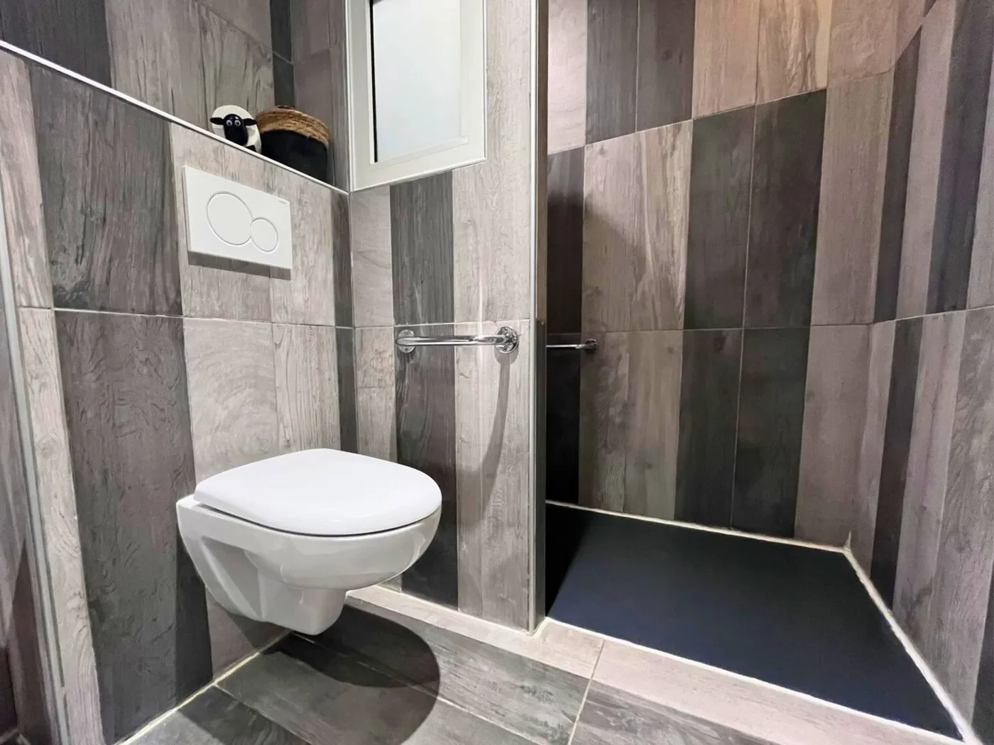Salle de bain accessible PMR avec douche à l'italienne, barres d'appui sécurisées et carrelage effet bois.