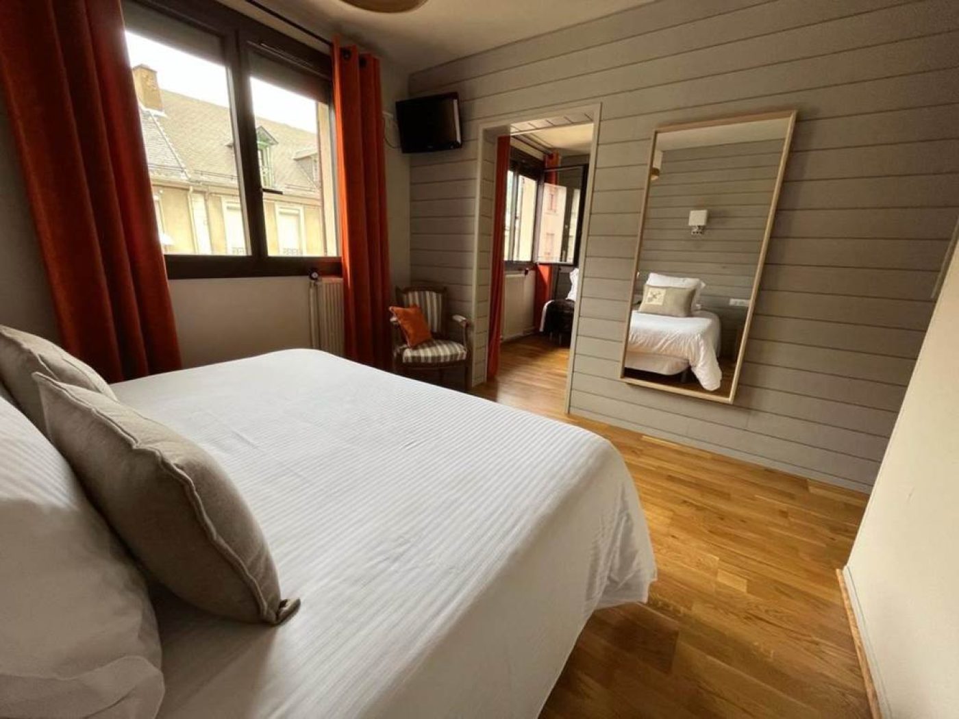Vue du côté droit du grand lit king-size de la chambre triple n°4 avec rideaux orange et murs en bois gris.