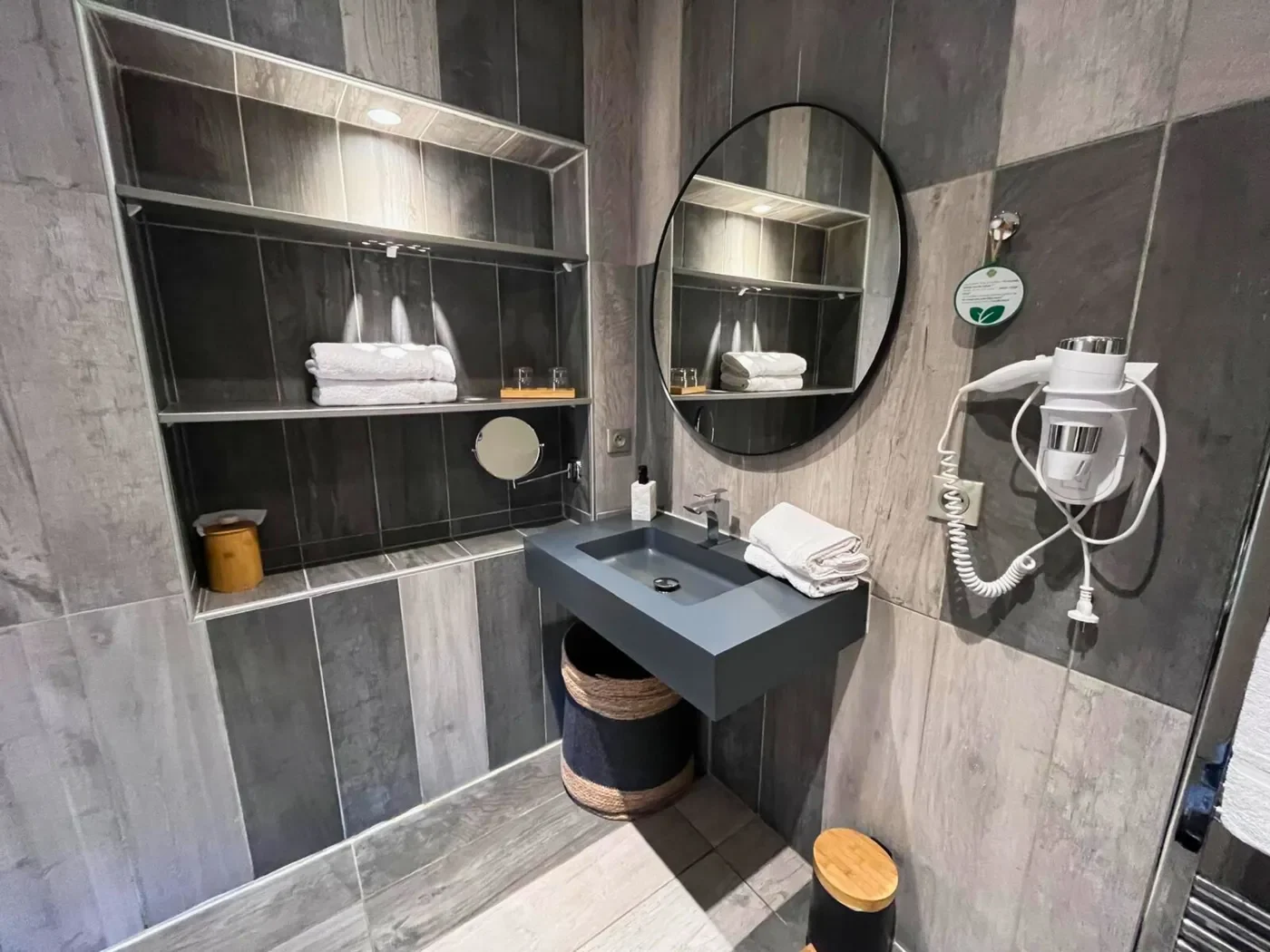 Lavabo suspendu accessible, miroir rond design et sèche-cheveux dans la salle de bain PMR.