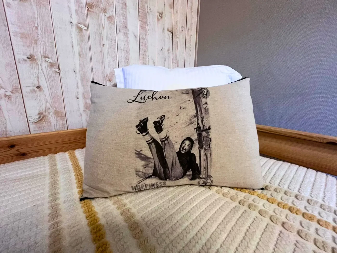 Coussin décoratif avec impression photographique ancienne de Luchon et inscription 'Happiness' sur le lit de la chambre 14.