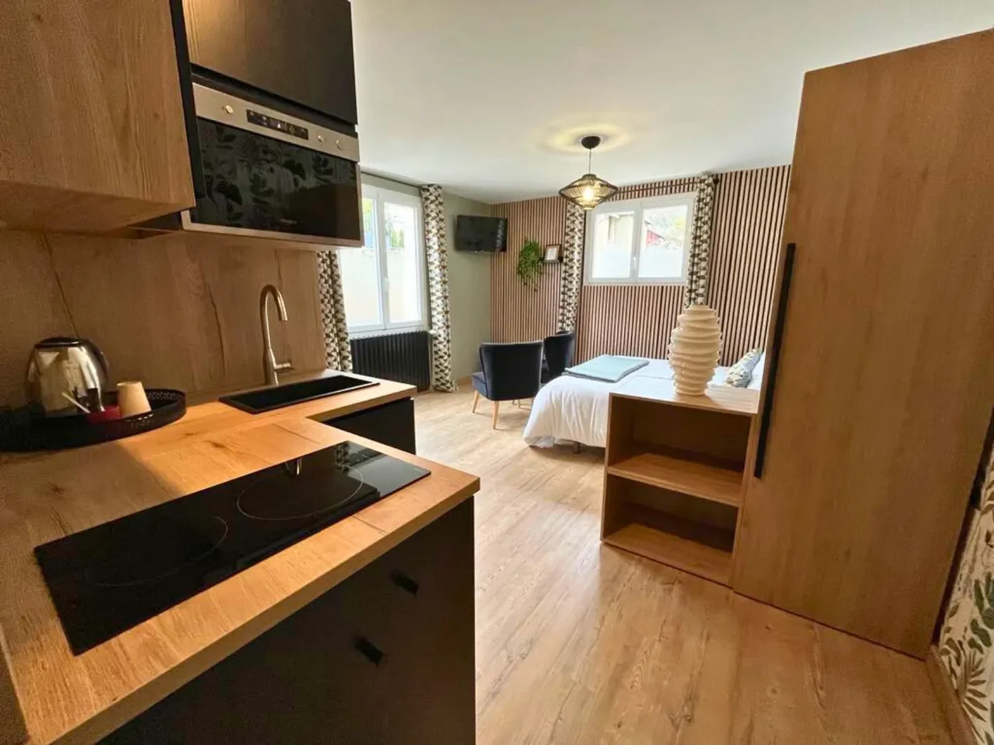 Détail de la cuisine équipée du studio avec plaques de cuisson à induction, évier noir, mobilier bois et électroménager moderne.