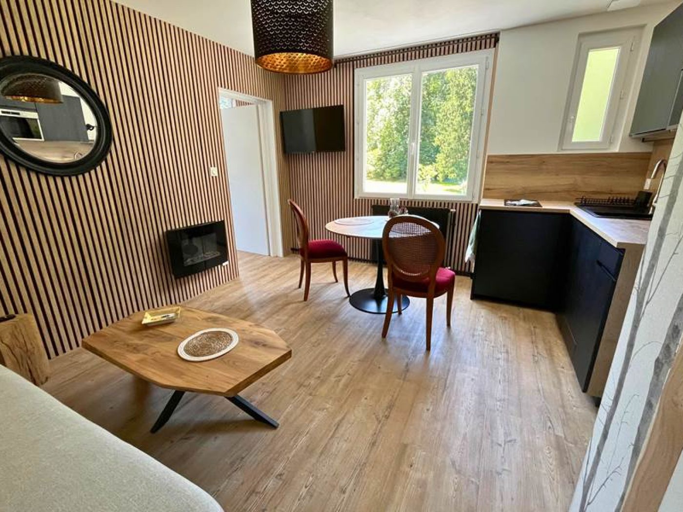 Vue de la kitchenette moderne de l'appartement T2 avec fenêtre, meubles en bois clair, plaques à induction et plateau de courtoisie.