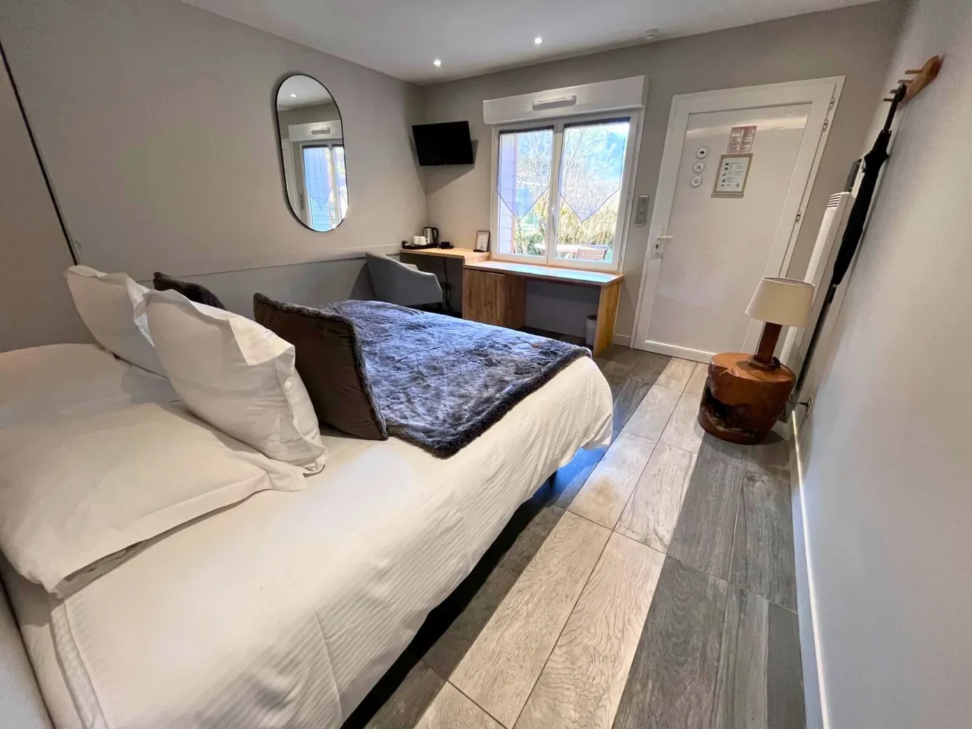 Intérieur de la chambre 25 avec bureau en bois clair, télévision et fenêtre donnant sur le jardin.