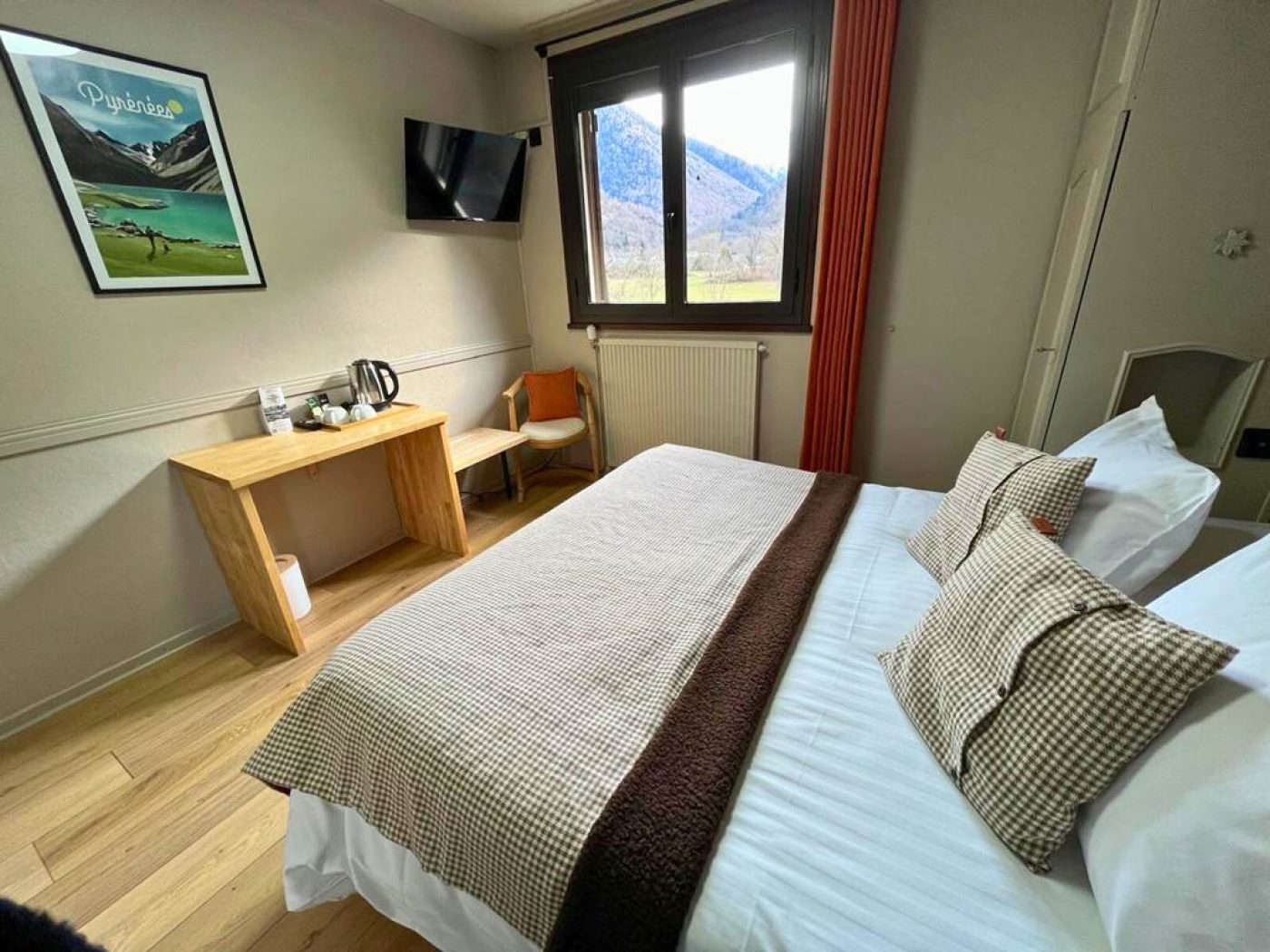 Vue depuis le lit de la chambre 9 mansardée, montrant la fenêtre donnant sur le jardin et les Pyrénées, avec la TV murale.