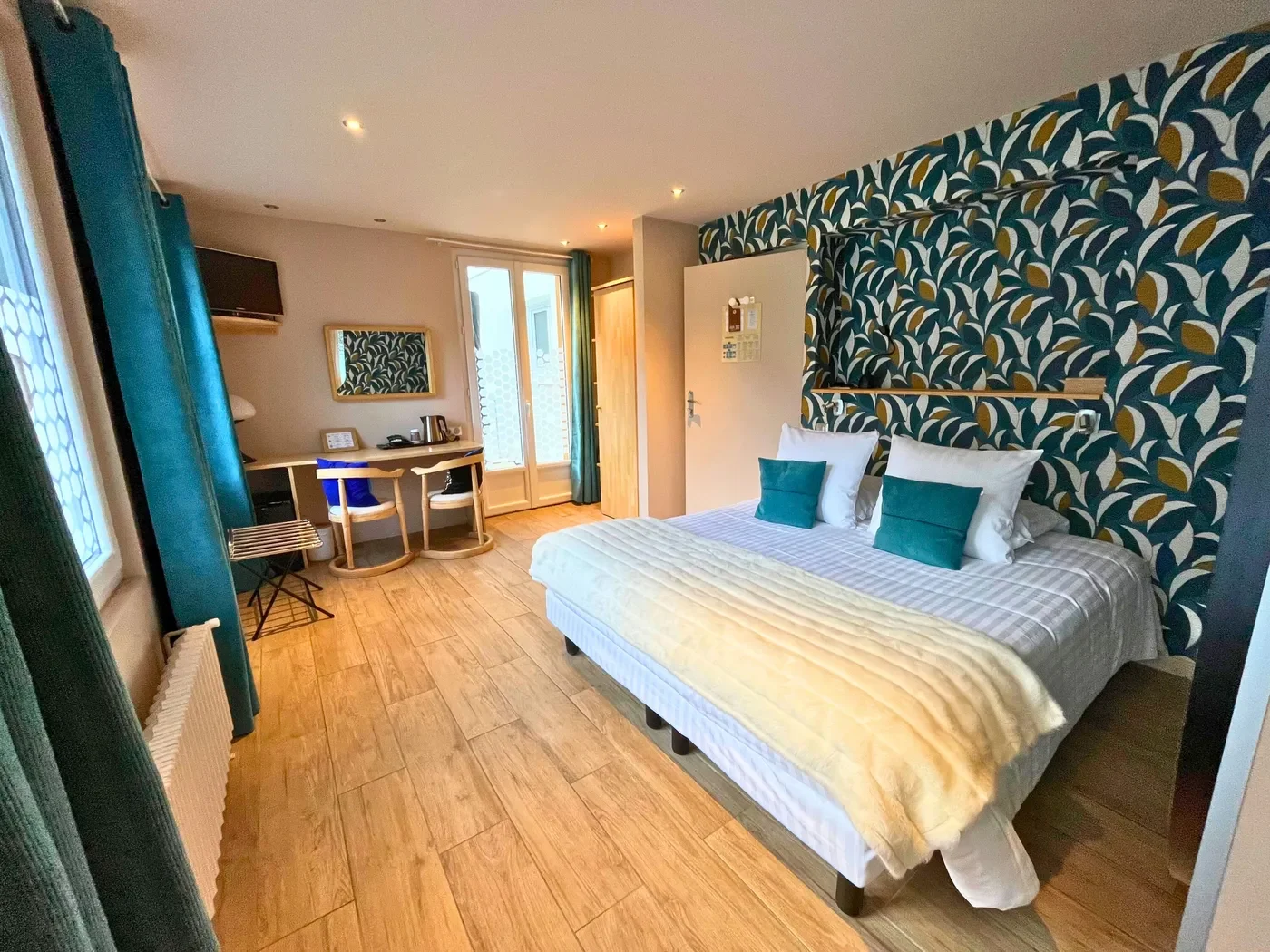 Vue globale de la chambre 32 avec lit queen-size, papier peint à motifs feuilles et accès terrasse.