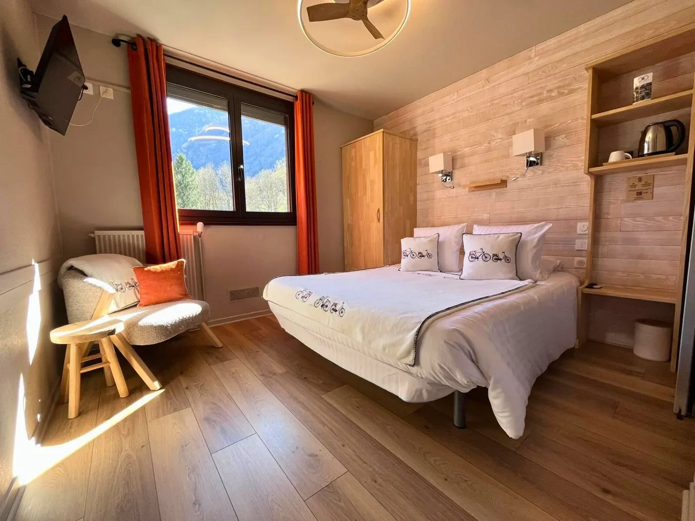 Vue d'ensemble de la chambre double n°8 cosy à l'Hôtel La Rencluse avec lit queen-size, rideaux orange et décor en bois clair.