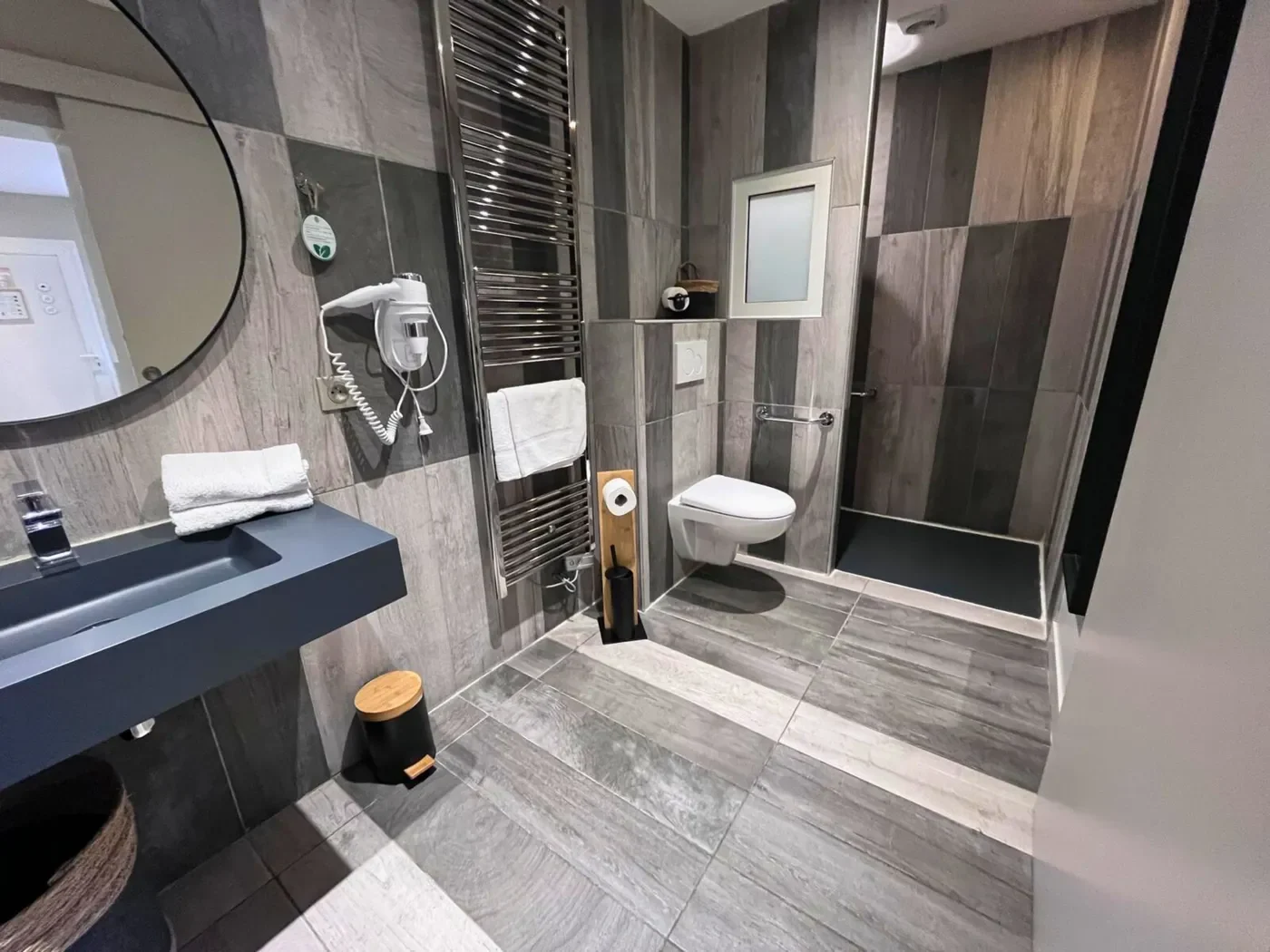 Vue d'ensemble de la salle de bain PMR avec grand sèche-serviettes chromé et douche italienne moderne.