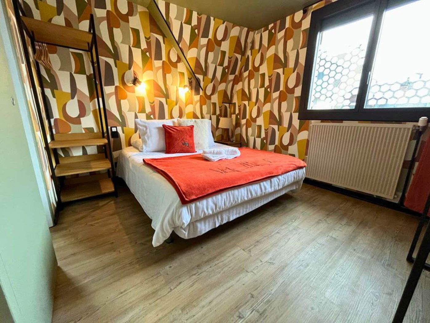Vue de face du lit queen-size de la chambre 10 avec mur en papier peint rétro et bureau boisé.