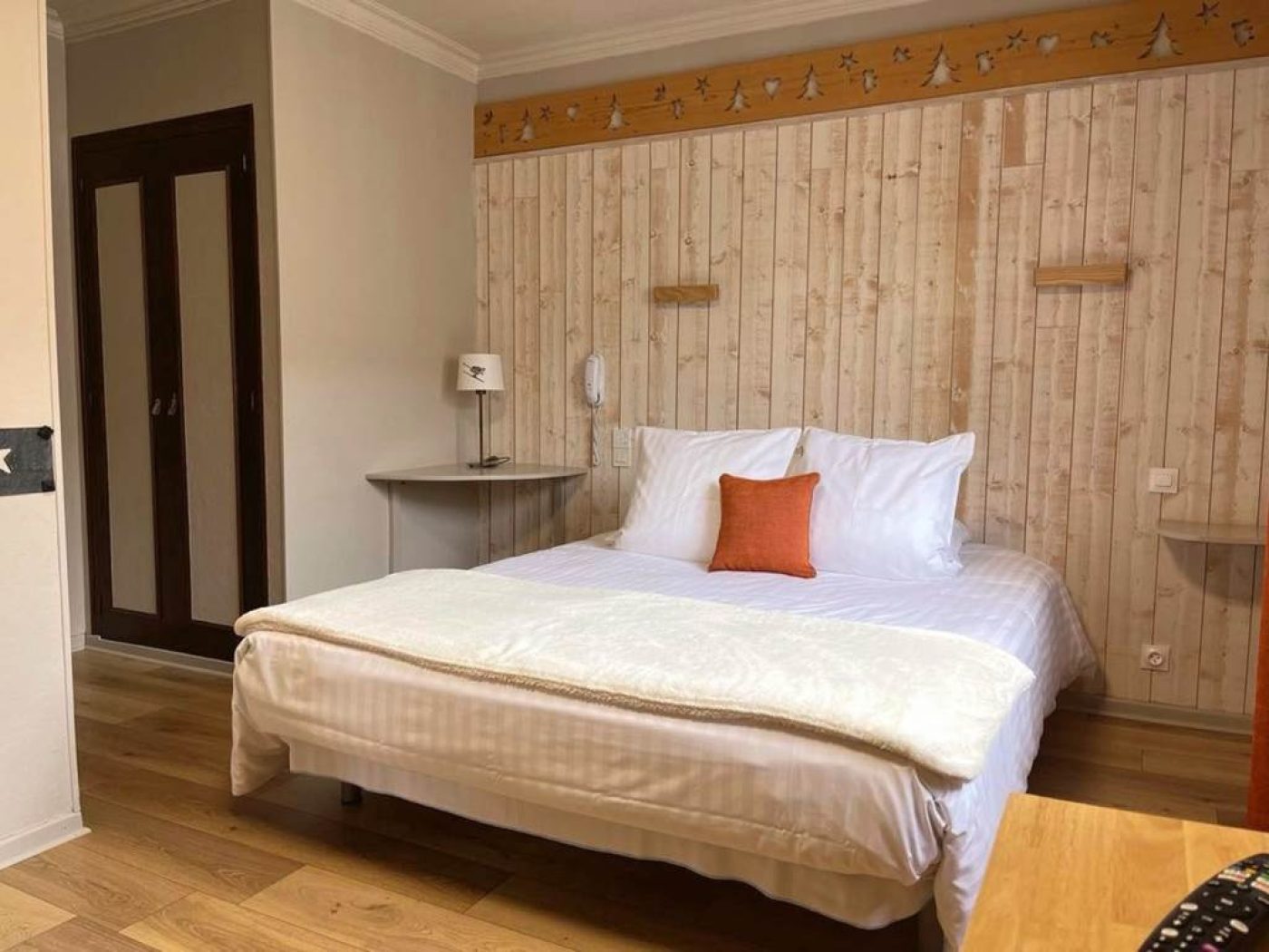Lit double queen-size de la chambre n°6 avec mur en bois clair sculpté d'une frise de sapins et placards de rangement intégrés.