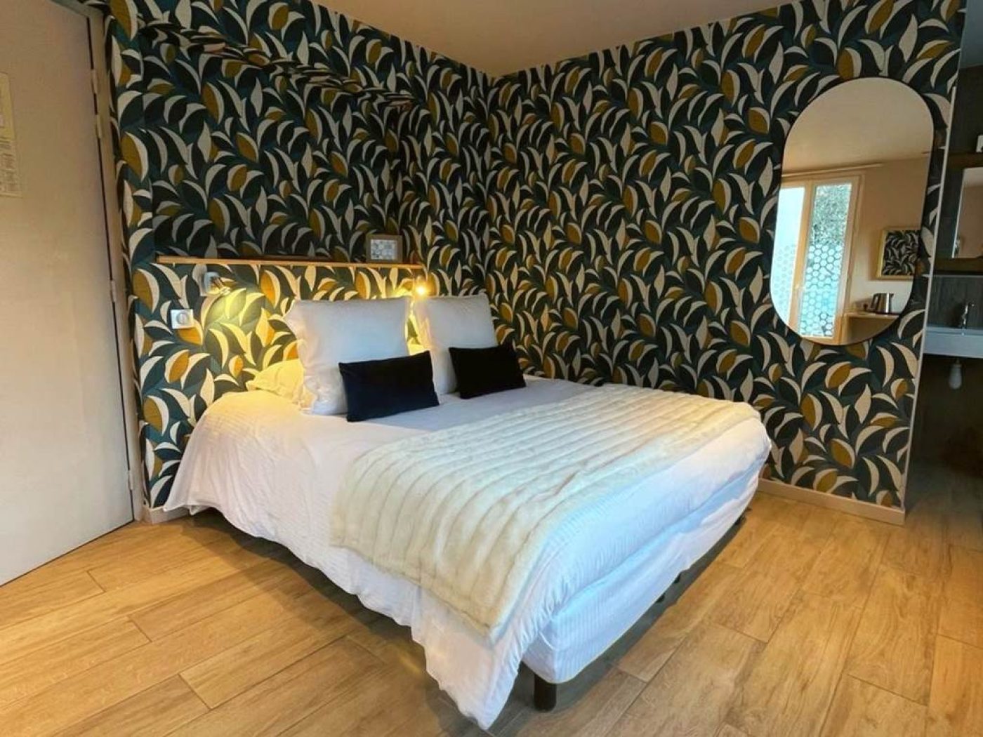 Lit double queen-size de la chambre 32 avec mur décoratif végétal et grand miroir en arche reflétant la pièce.