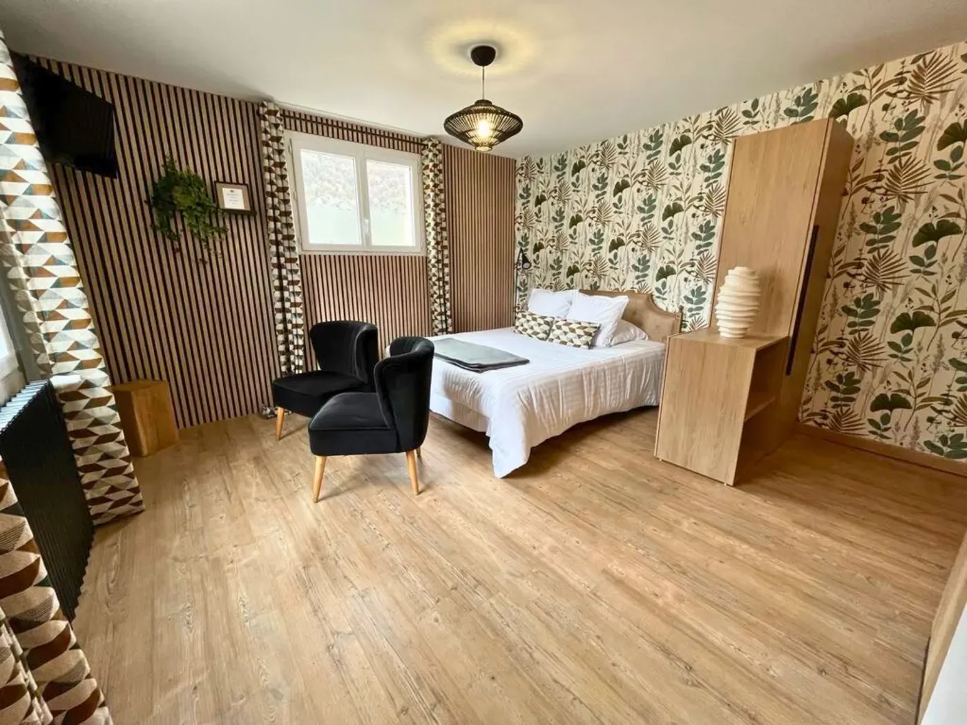 Perspective du studio depuis l'entrée montrant le papier peint panoramique à motifs fougères, le lit queen-size et les rangements en bois.