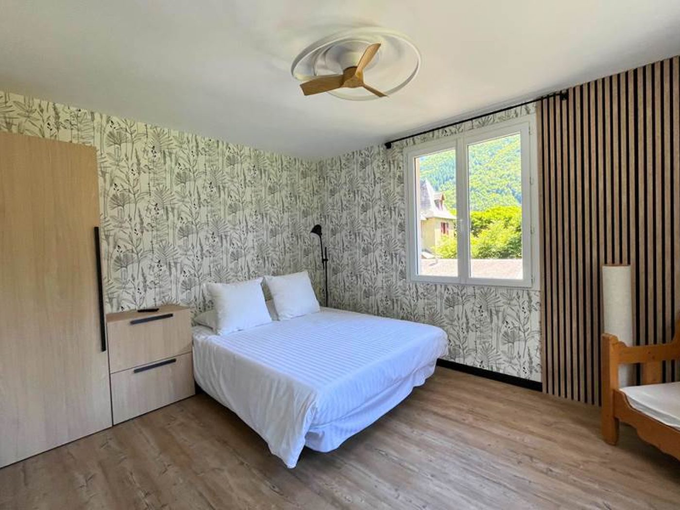 Lit double préparé avec linge de lit blanc et mur boisé chaleureux dans la chambre du T2.