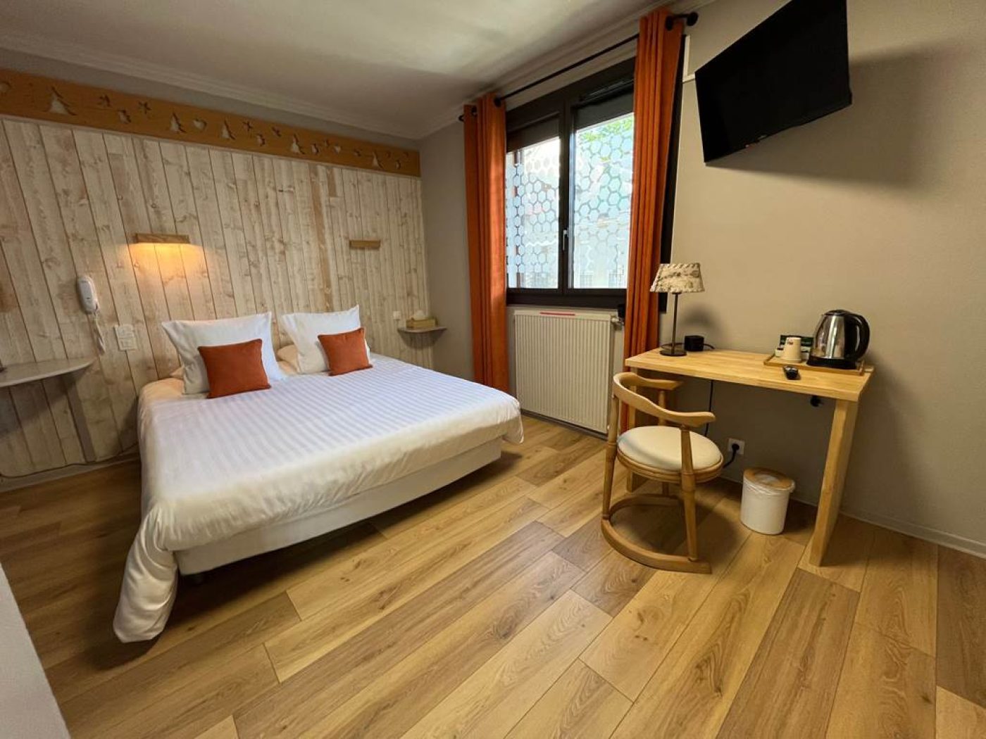 Coin bureau en bois clair avec fauteuil design, plateau de courtoisie et télévision murale dans la chambre 6.