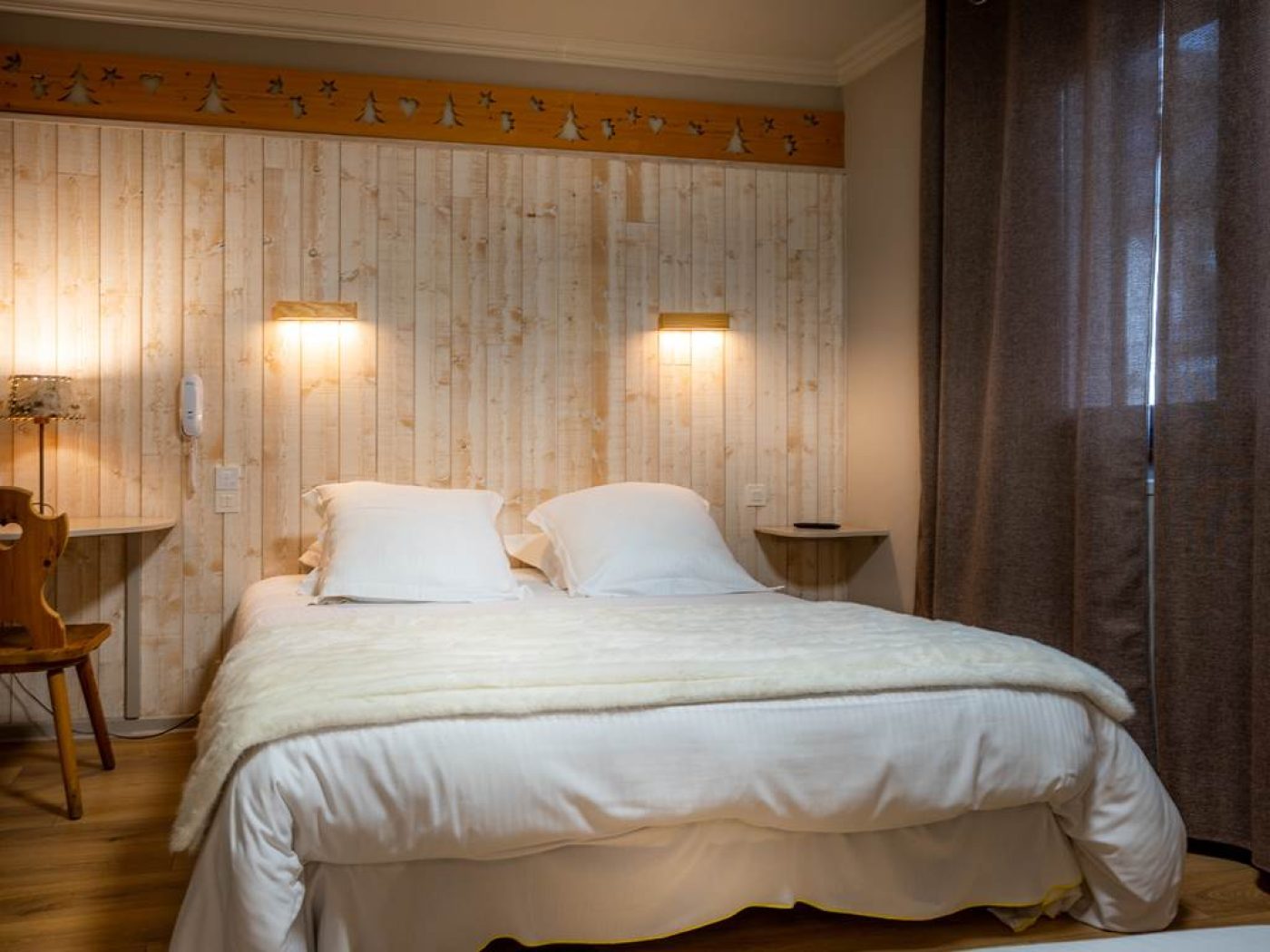 Lit double queen-size de la chambre 14 avec mur en bois blond et frise artisanale sculptée.