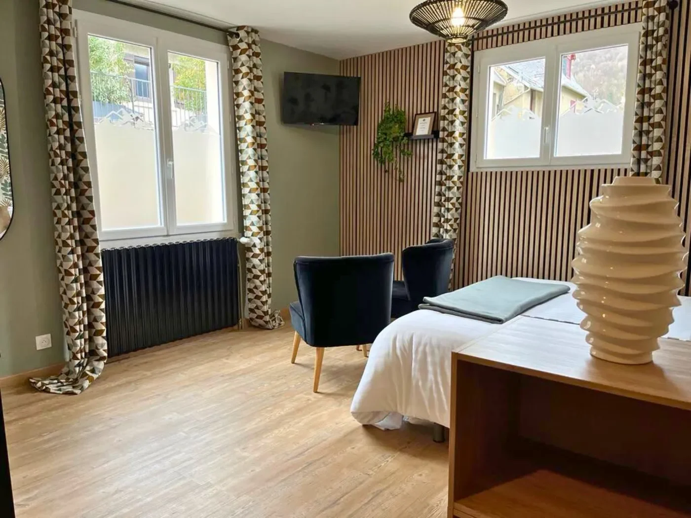 Espace de vie lumineux du studio avec fenêtres, mur en tasseaux de bois, fauteuils velours et télévision murale.