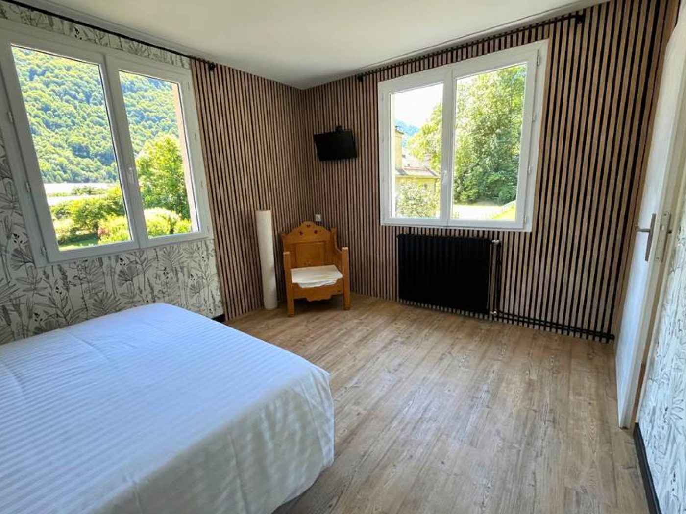 Chambre séparée de l'appartement T2 avec lit queen-size, rideaux orange et fenêtre ouvrant sur le jardin.
