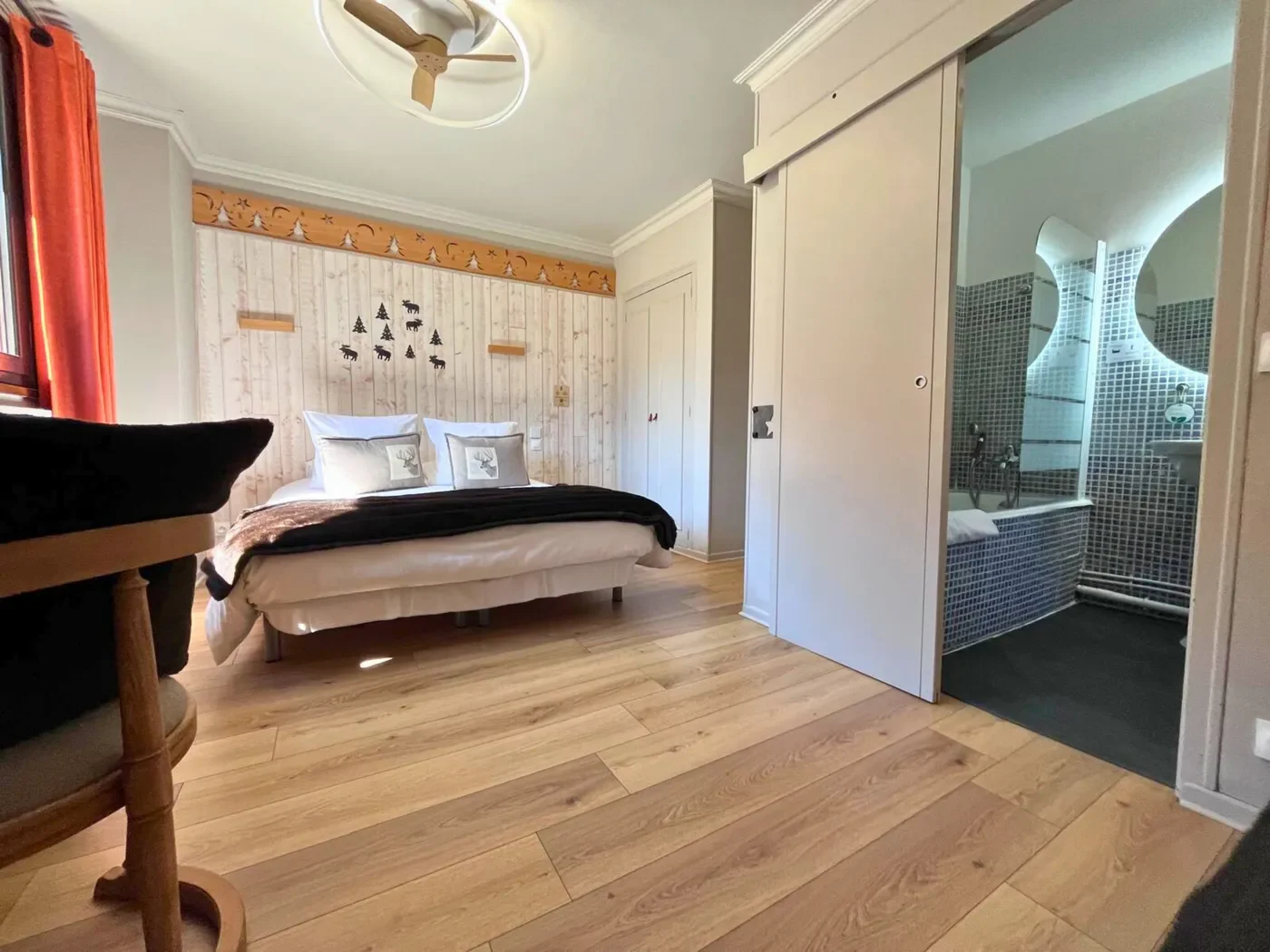 Perspective depuis le lit queen-size vers la salle de bain privative et le ventilateur de plafond au design bois.