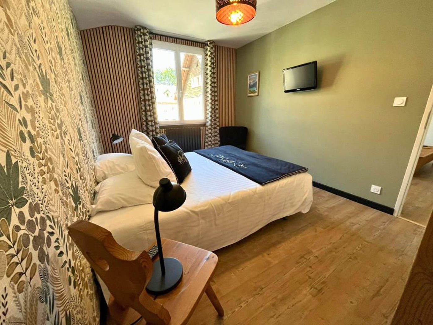 Chambre principale de l'appartement T3 avec grand lit double, télévision écran plat murale et décoration boisée.