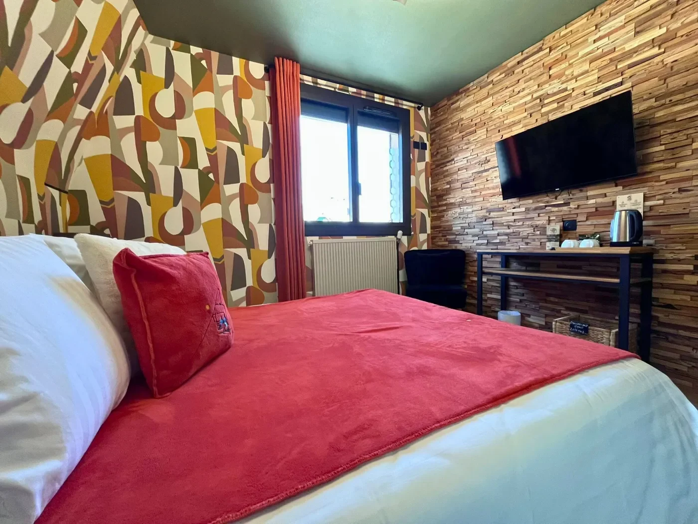 Chambre double n°10 avec lit queen-size rouge, mur de bois massif, papier peint vintage et TV écran plat.