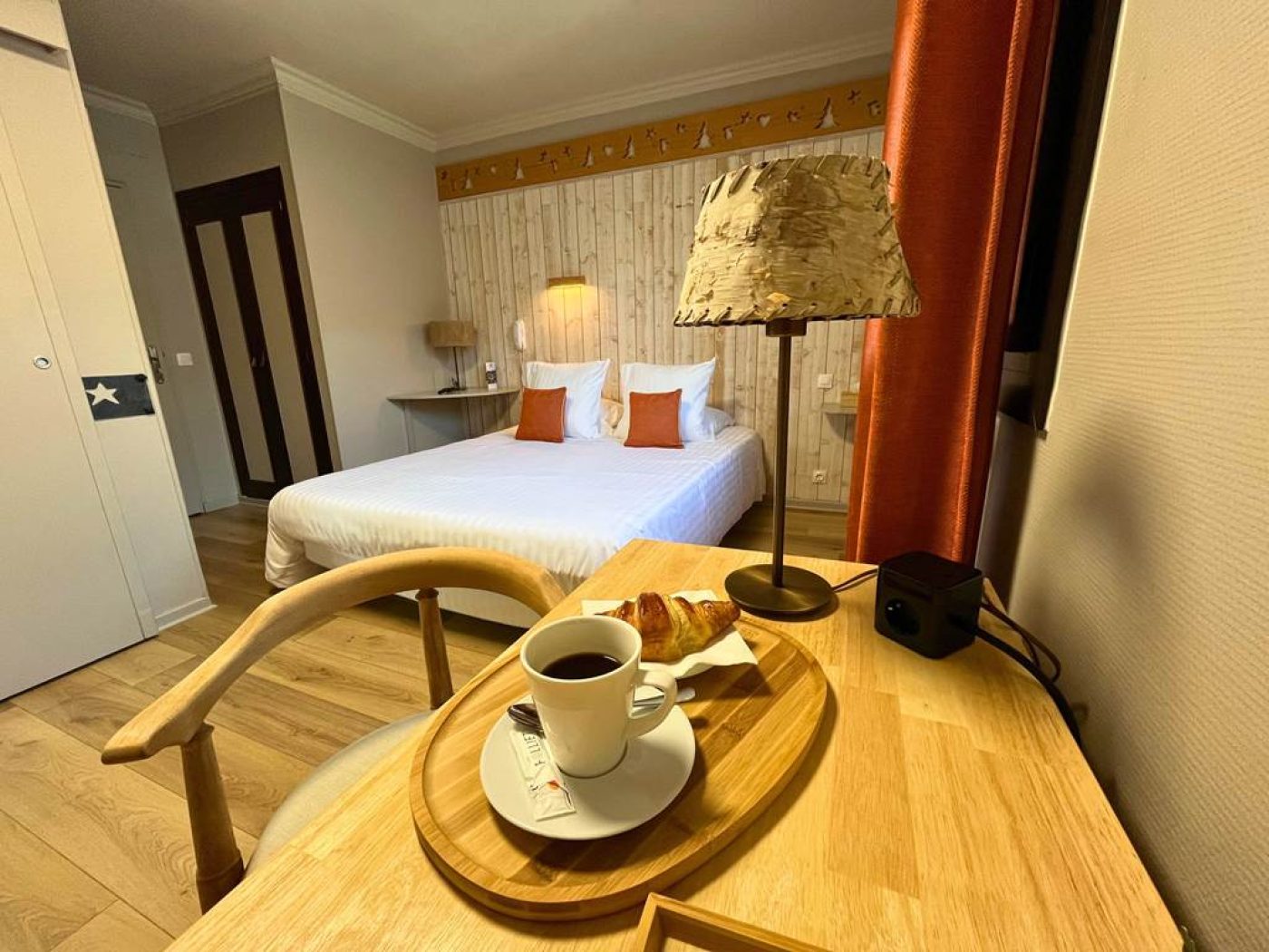 Petit-déjeuner servi en chambre triple avec café et croissant sur un plateau en bois devant le lit king-size.
