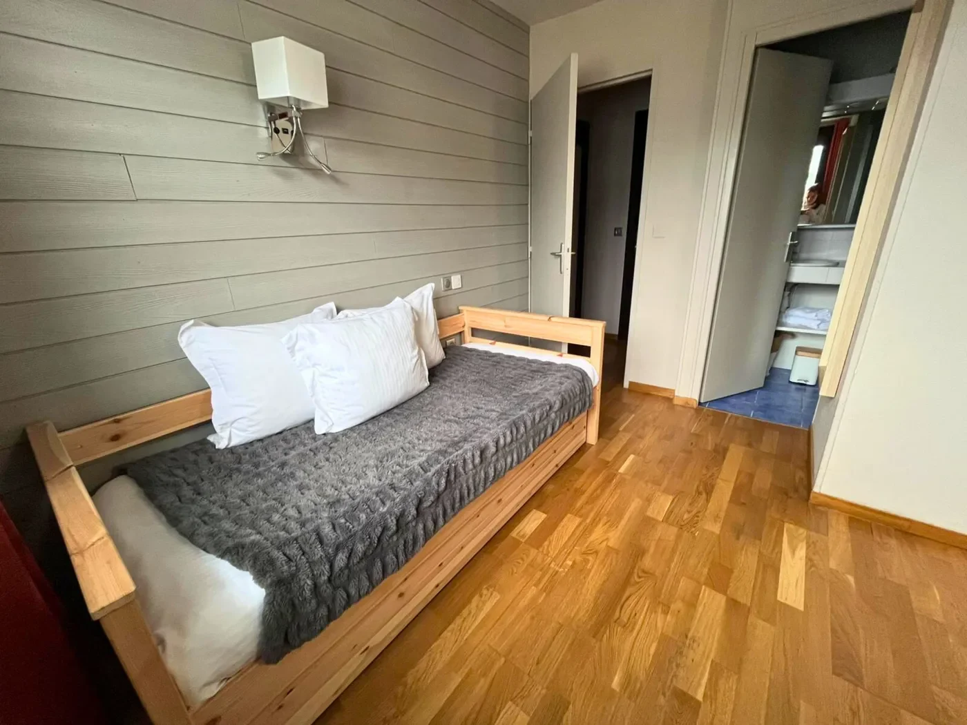 Espace lit simple 90x200 dans la chambre triple n°11 avec mur en bois clair et plaid gris anthracite.
