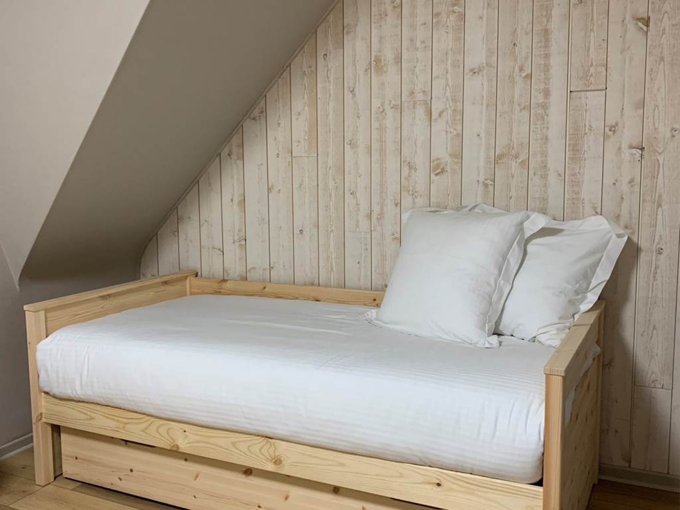 Zoom sur le lit simple 90x200 avec linge de lit blanc et mur boisé dans la chambre triple 14.