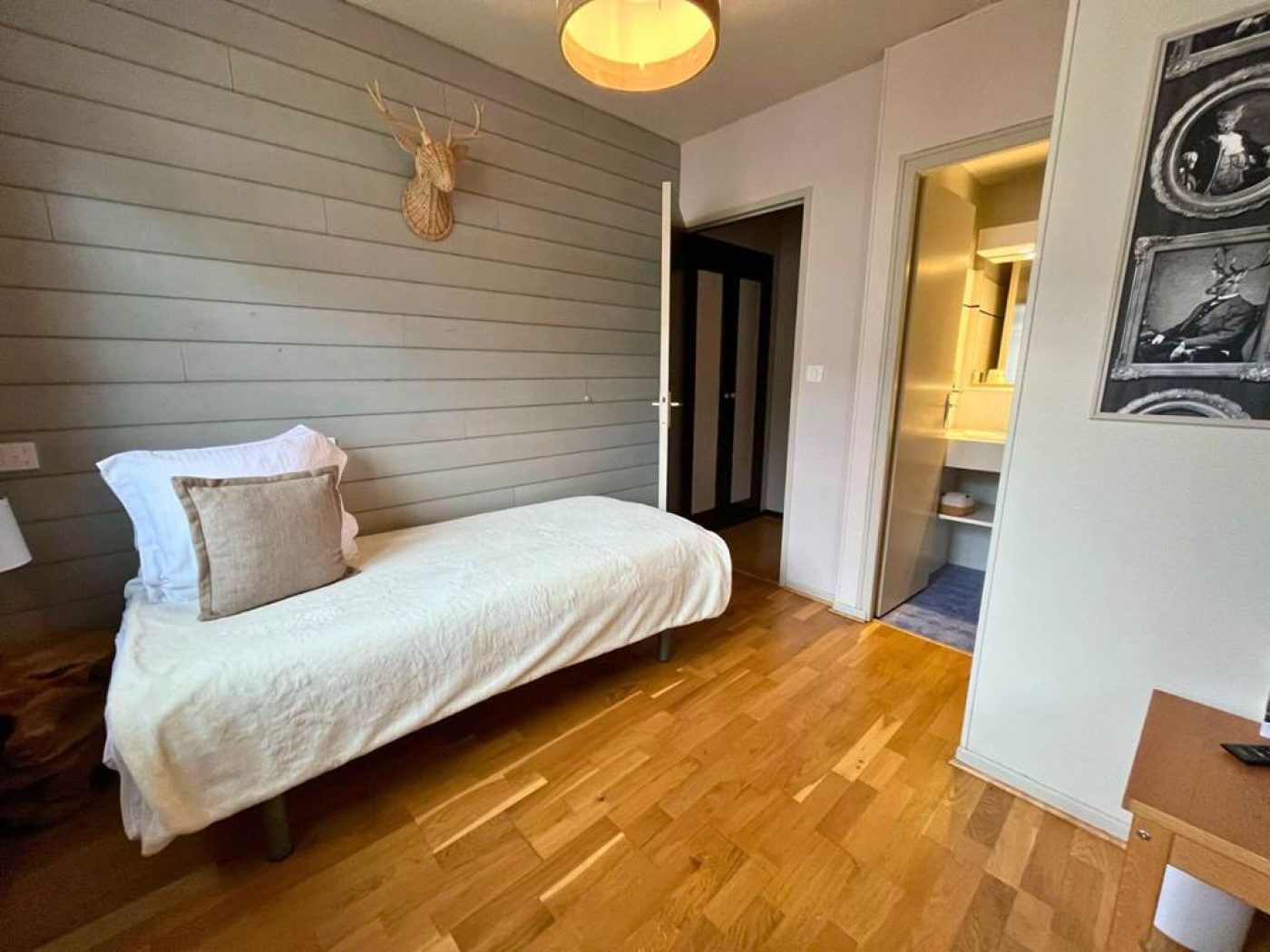 Zoom sur le lit simple 90x200 avec coussin tête de cerf et accès à la seconde salle d'eau.