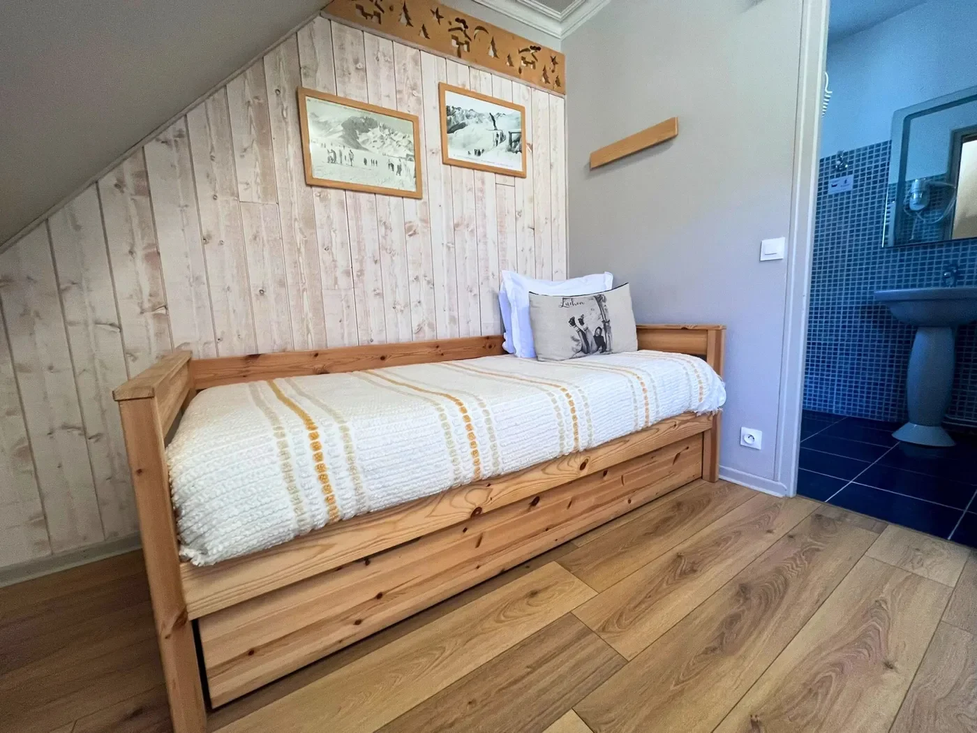 Coin nuit avec lit simple sous mansarde, mur en bois clair et cadres vintage de la station de Superbagnères en chambre 14.