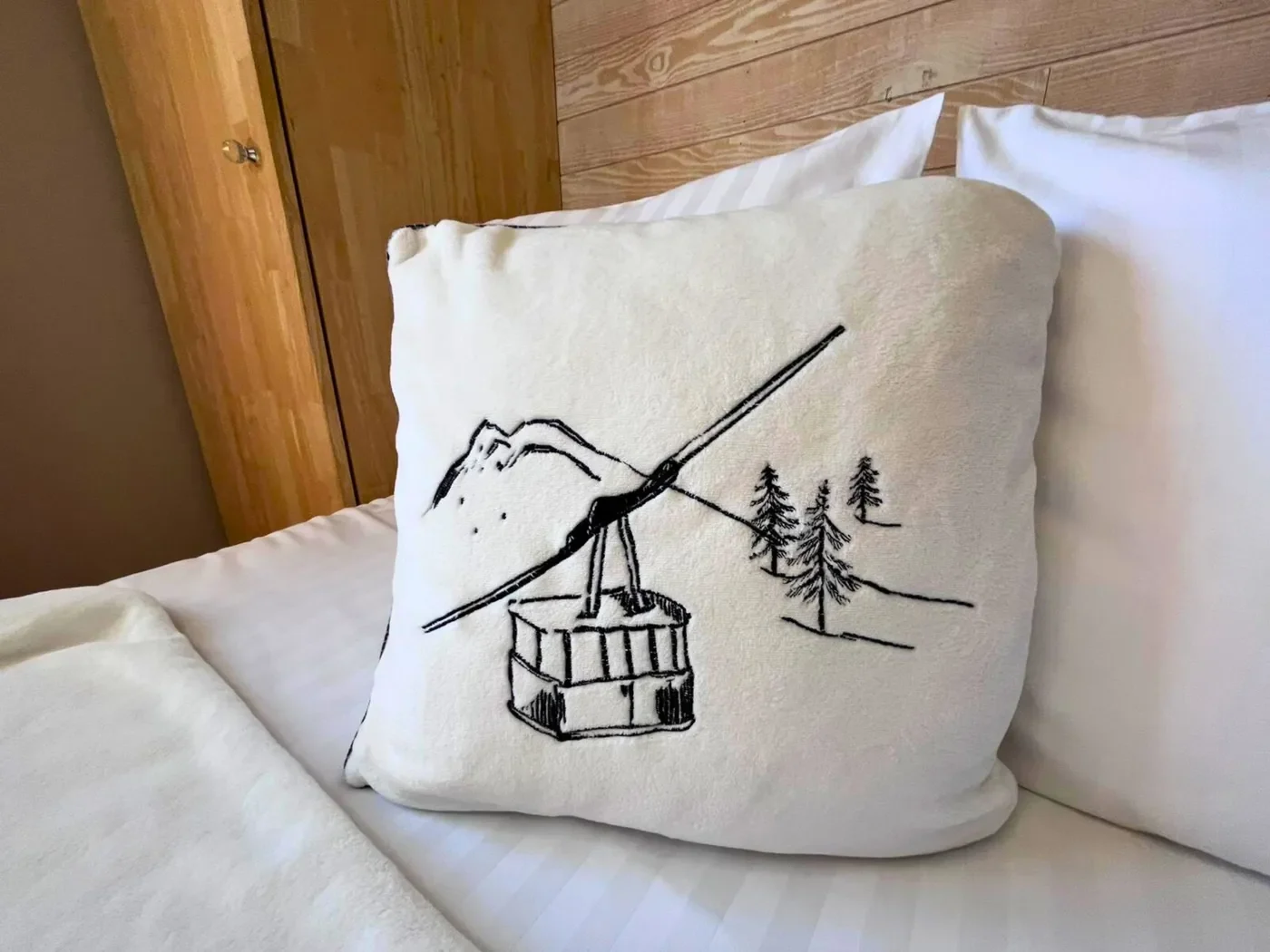 Détail de la literie haut de gamme de l'Hôtel La Rencluse avec oreiller brodé motif téléphérique et montagnes, ambiance boisée chaleureuse.