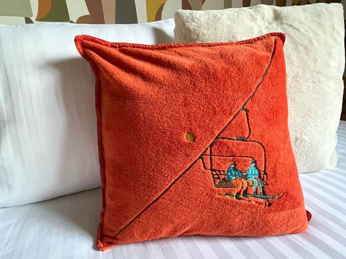 Détail d'un oreiller en velours orange brodé avec un motif de télésiège dans la chambre 10.