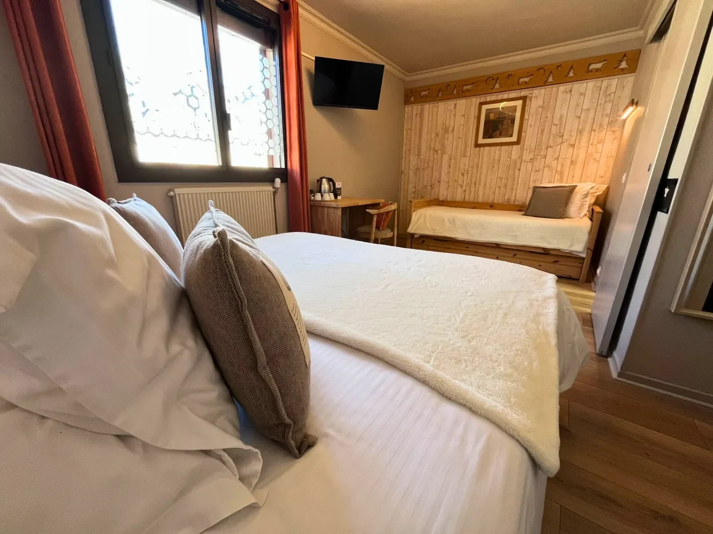 Vue perspective de la chambre 6 montrant le lit king-size, le lit simple au fond et les rideaux orange.