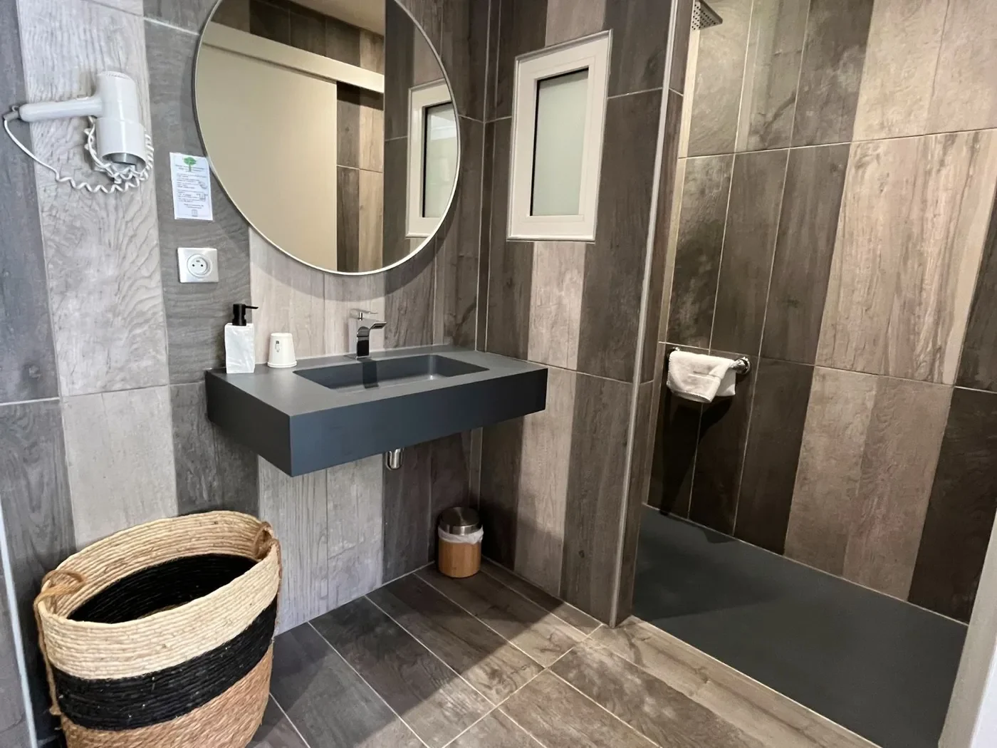 Salle de bain moderne de la chambre 31 avec douche à l'italienne, vasque grise suspendue et miroir rond rétro-éclairé.