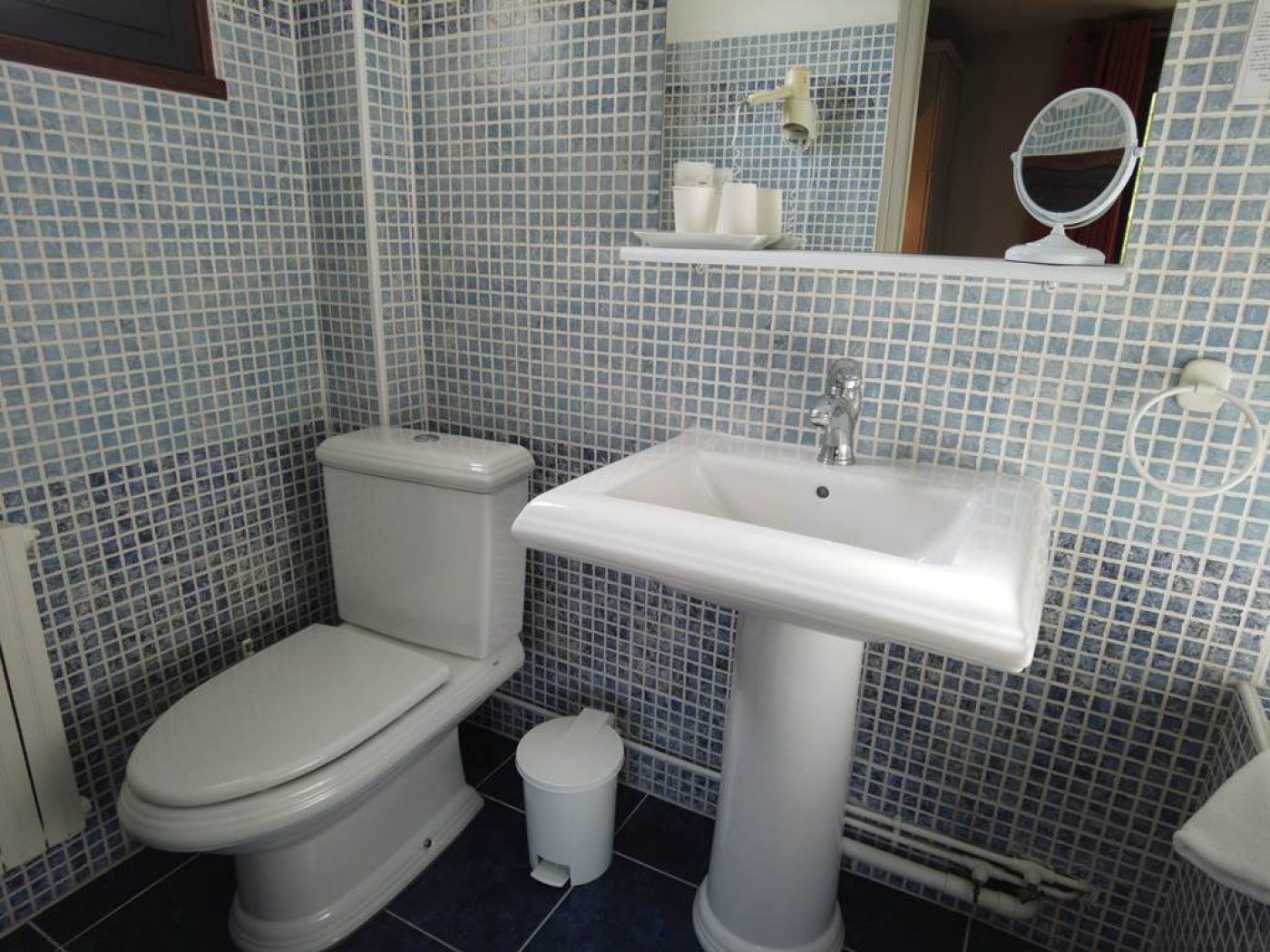 Salle de bain privative mansardée de la chambre 9 avec lavabo, miroir rond, baignoire-sabot sous pente et douchette géothermale.