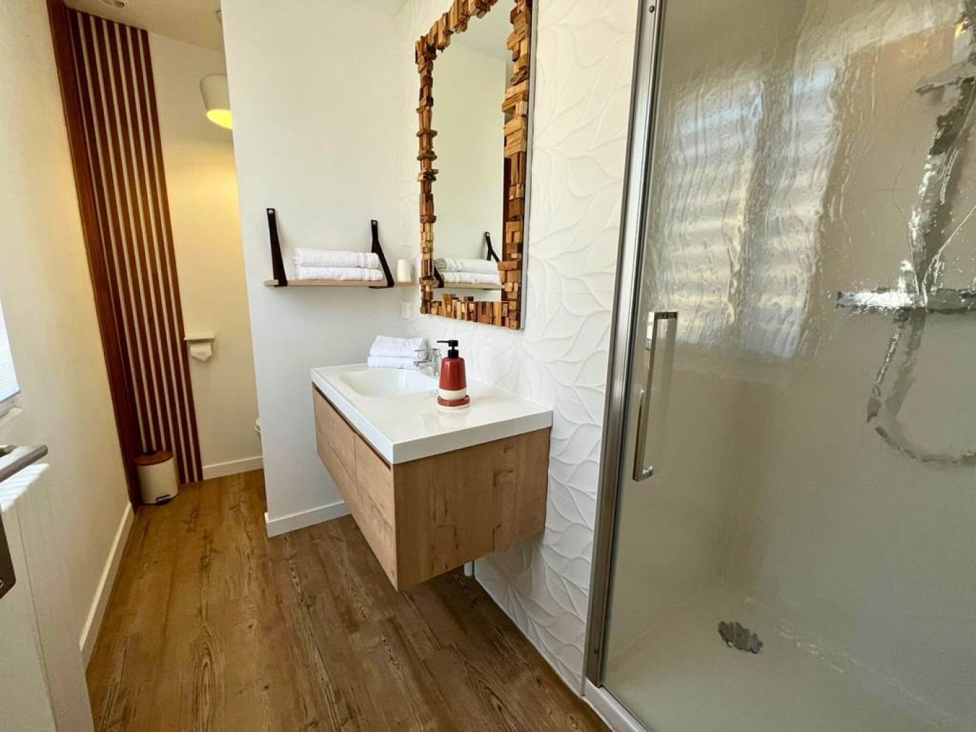 Salle de bain rénovée de l'appartement T3 avec douche, vasque moderne blanche et carrelage effet pierre.