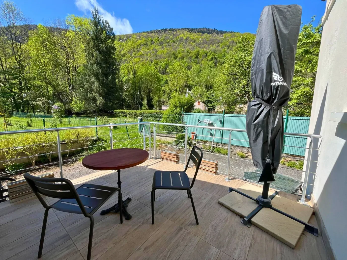 Terrasse privative de la chambre 32 avec table, chaises noires et parasol donnant sur un jardin boisé.